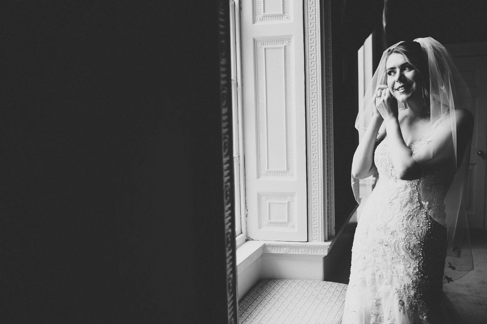 Colwick Hall wedding photography - bride puts on earrings in front of window
