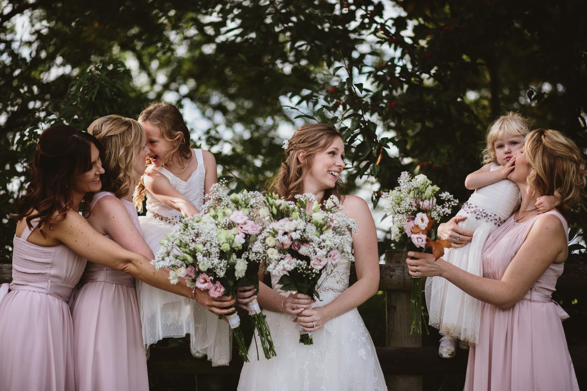 Bride with bridesmaids laughing with each other in front of trees