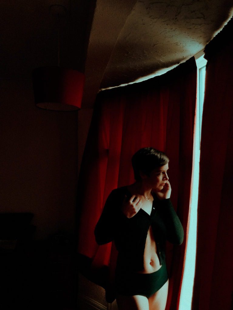 The Photographer, photographed by Tim Dunk in a virtual photoshoot, in cardigan and knickers looking out of window.