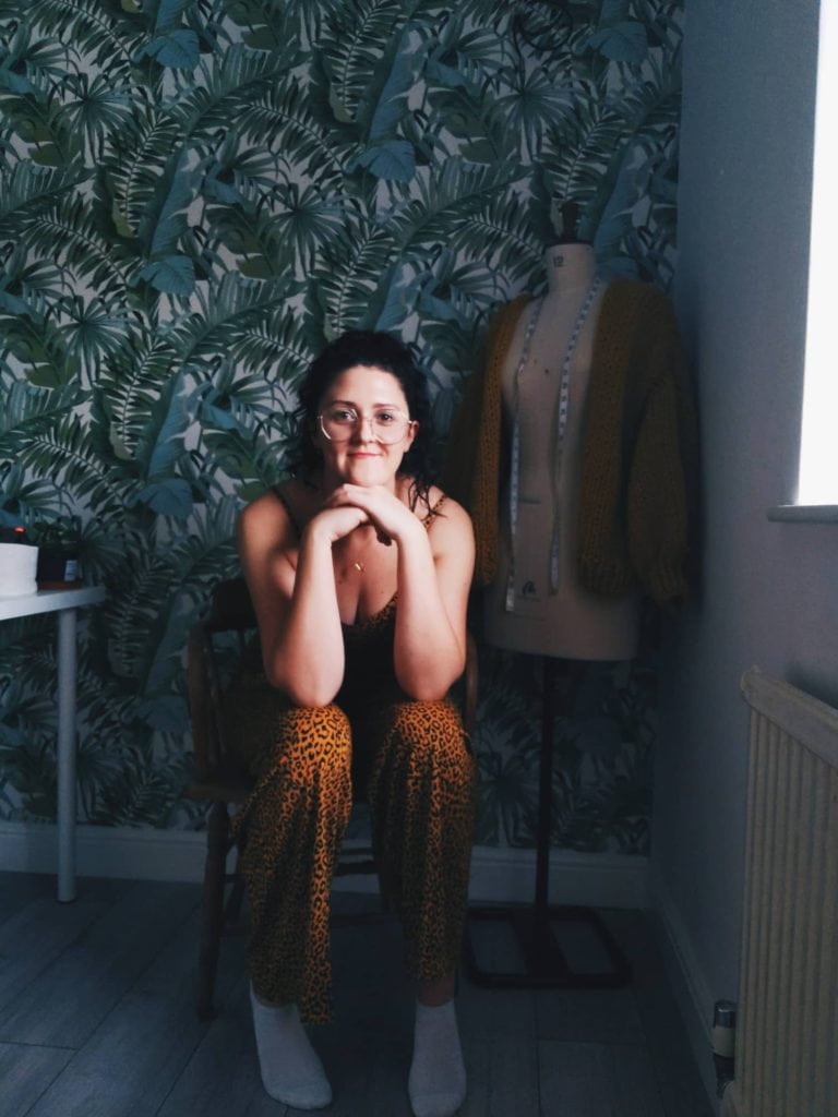 Sammi sitting on her chair next to clothing manikin in her sewing room in a virtual photoshoot