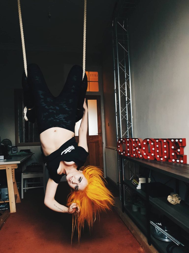 Kate hanging upside down on a trapeze, flame orange hair. In a virtual photoshoot via iPhone