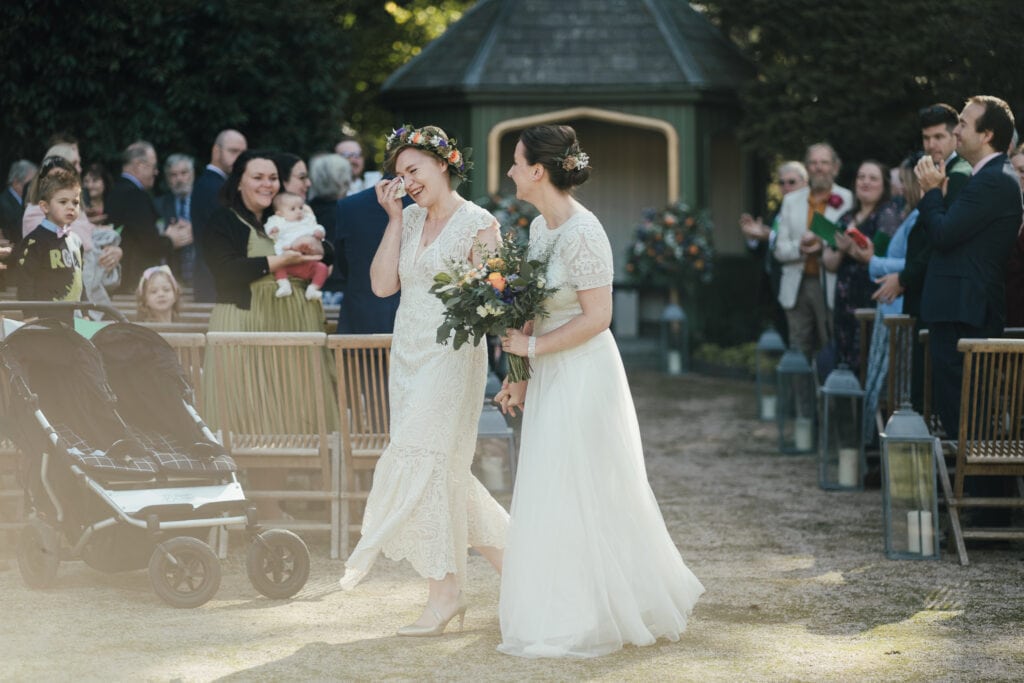 Wedding Photography at Thorpe Garden. Brides walking out of ceremony. One bride with tissue to eyes. Happy tears.