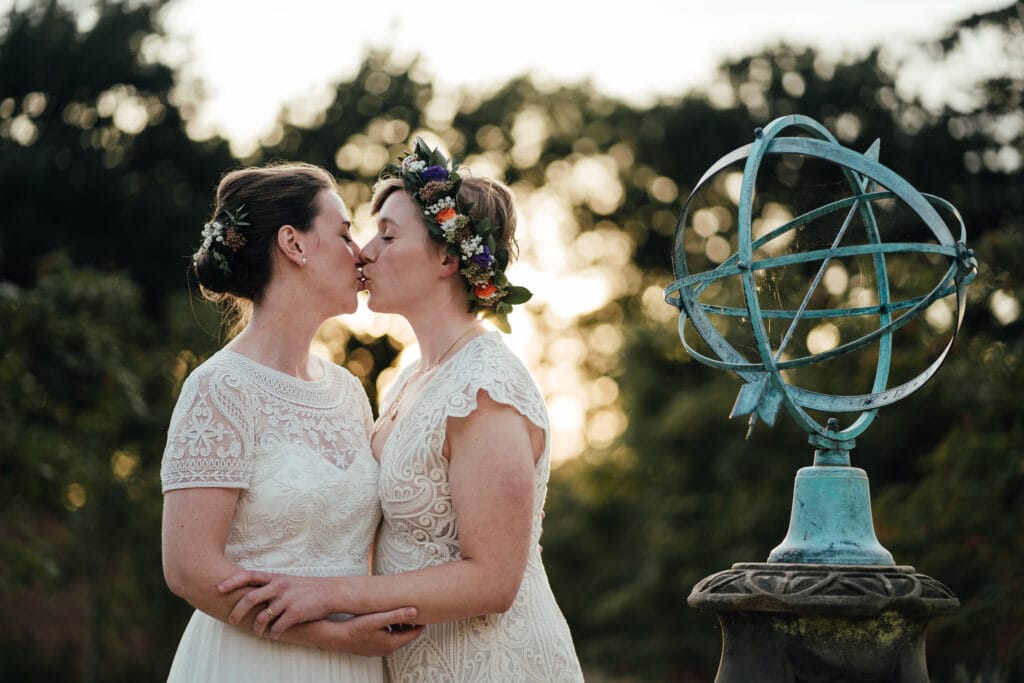 Brides kiss in the evening sunlight next to sundial at Thorpe Garden.