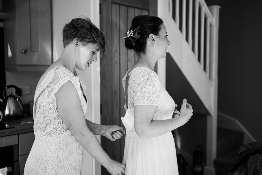 Black and white photo of Bride and Bride helping each other get ready. Doing up each others wedding dress.