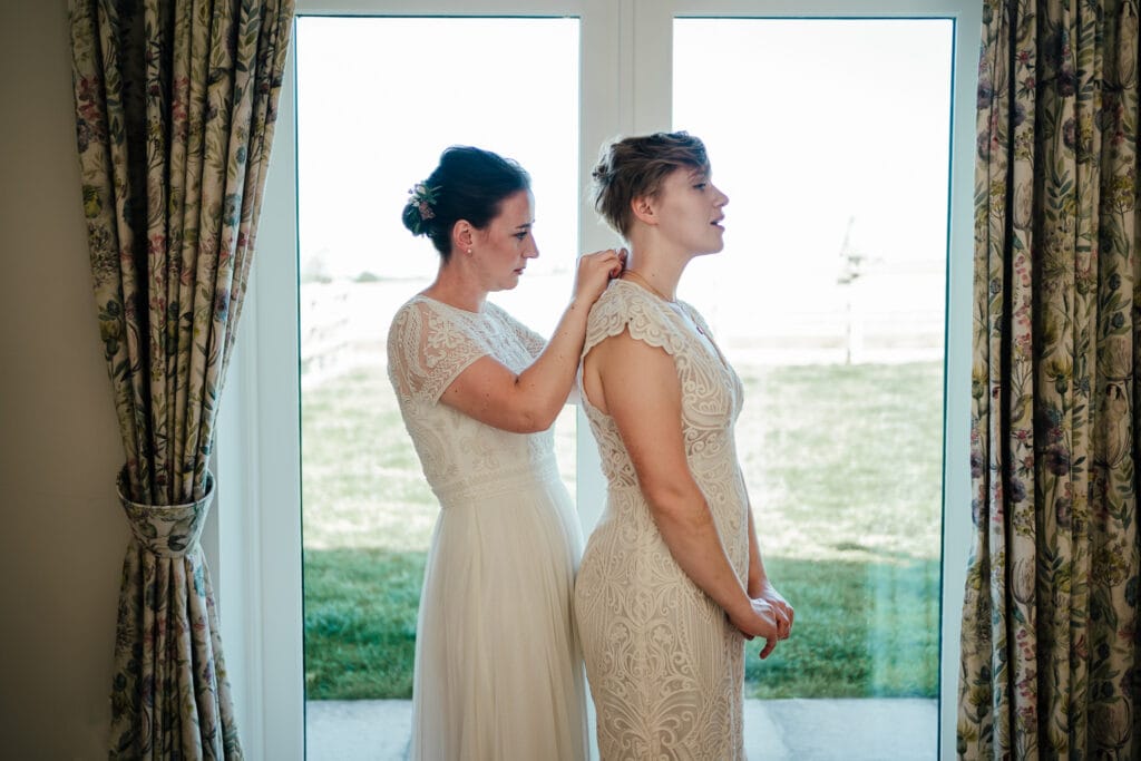 Millie doing up Alex's dress in the window
