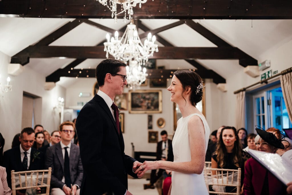 Wedding photography at Widbrook Grange : Bride and groom look at each other holding hands and smiling in ceremony