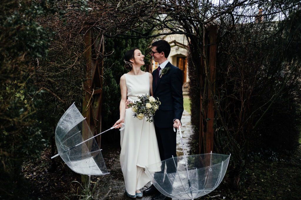 Wedding photography at Widbrook Grange: Bride and groom look at each other, holding open clear brollies by their side