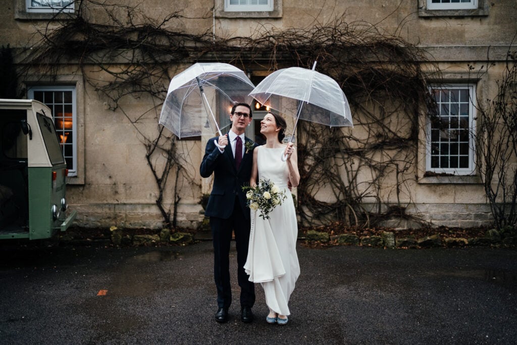 Bride and groom outside Widbrook Grange, holding brollies above their head , bride looking up