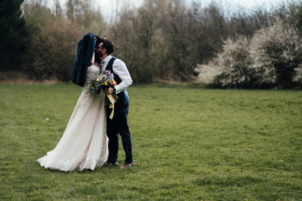 Bride and groom kiss in the rain at the Hidden Hive wedding venue. Surrounded by woodland