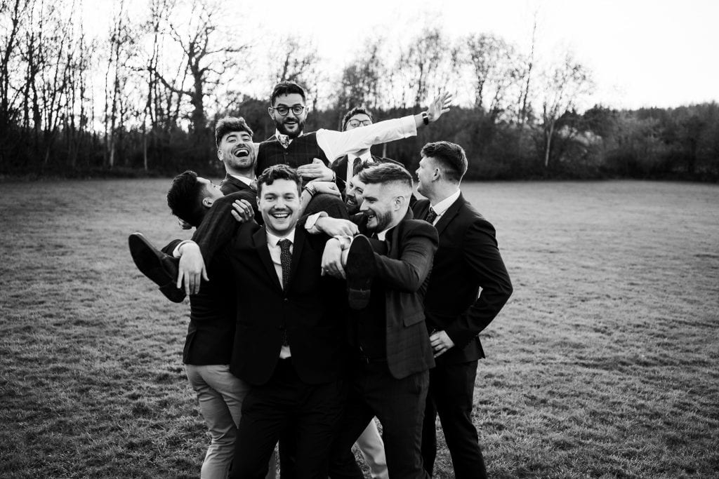 black and white of groom being carried by groomsmen