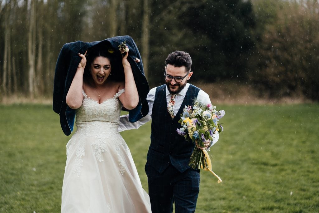 Bride holds groom's jacket over her head in the rain