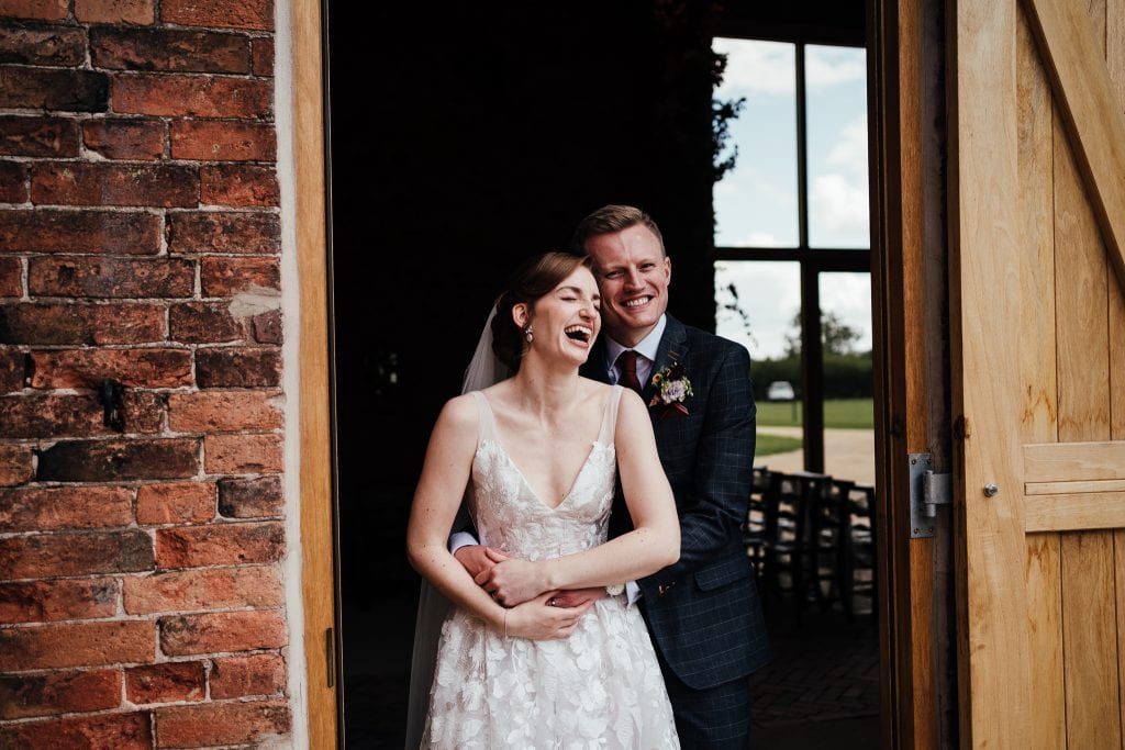 Bride and groom standing in doorway at The Mill Hoveringham. Bride is laughing. Groom has his arms around the bride