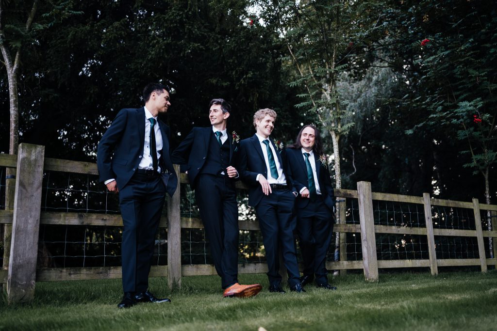 Groom and groomsmen leaning against the fence at Hazel Gap Barn.