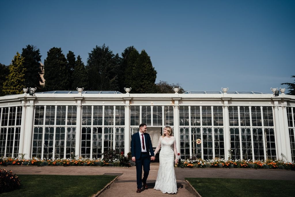 Wollaton Park Wedding - bride and groom walk down the path from Camellia house. the greenhouse in the background