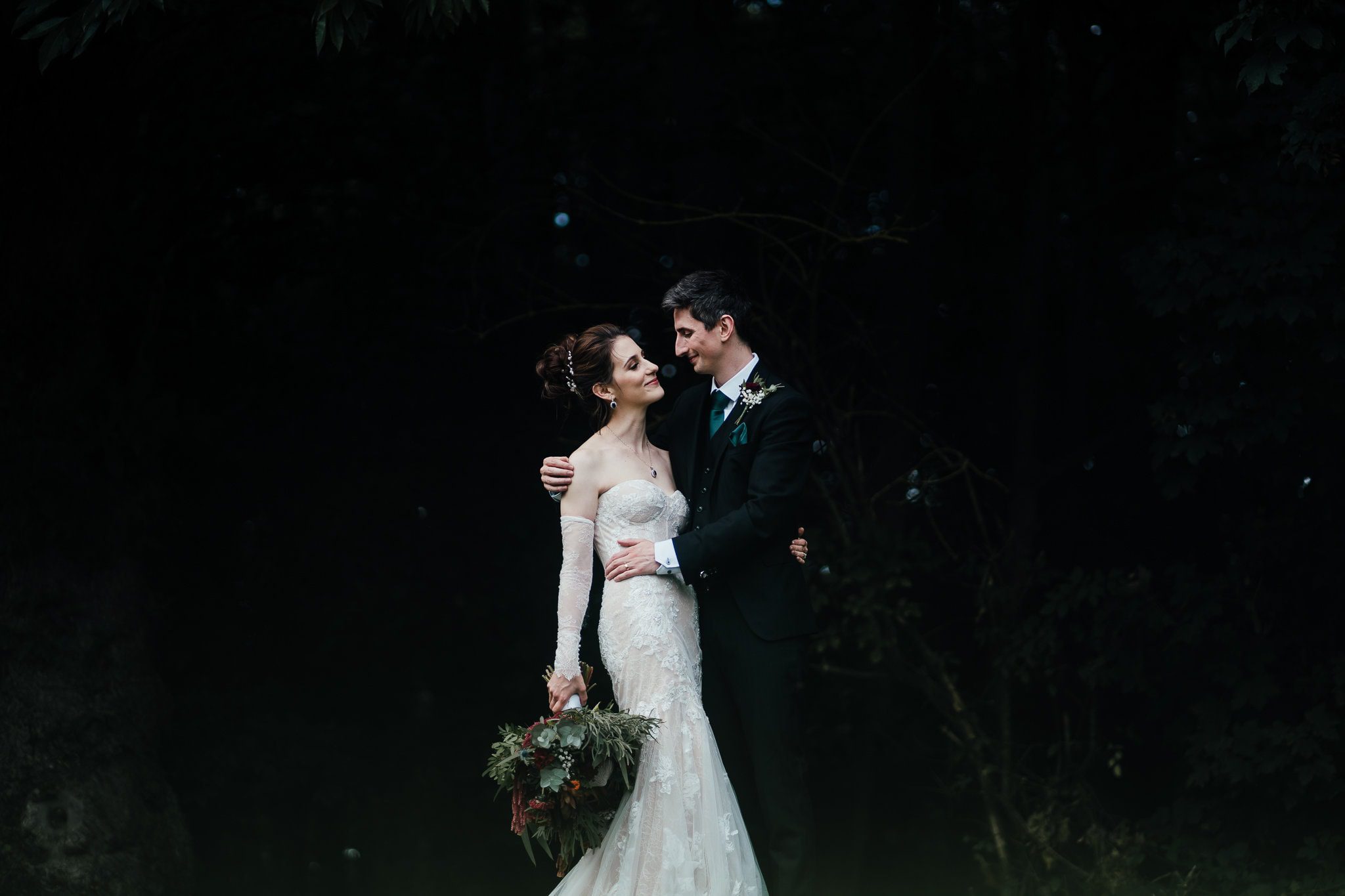 Bride and groom at Hazel Gap Barn. Looking at each other. Lit beautifully against the dark background of the woods.