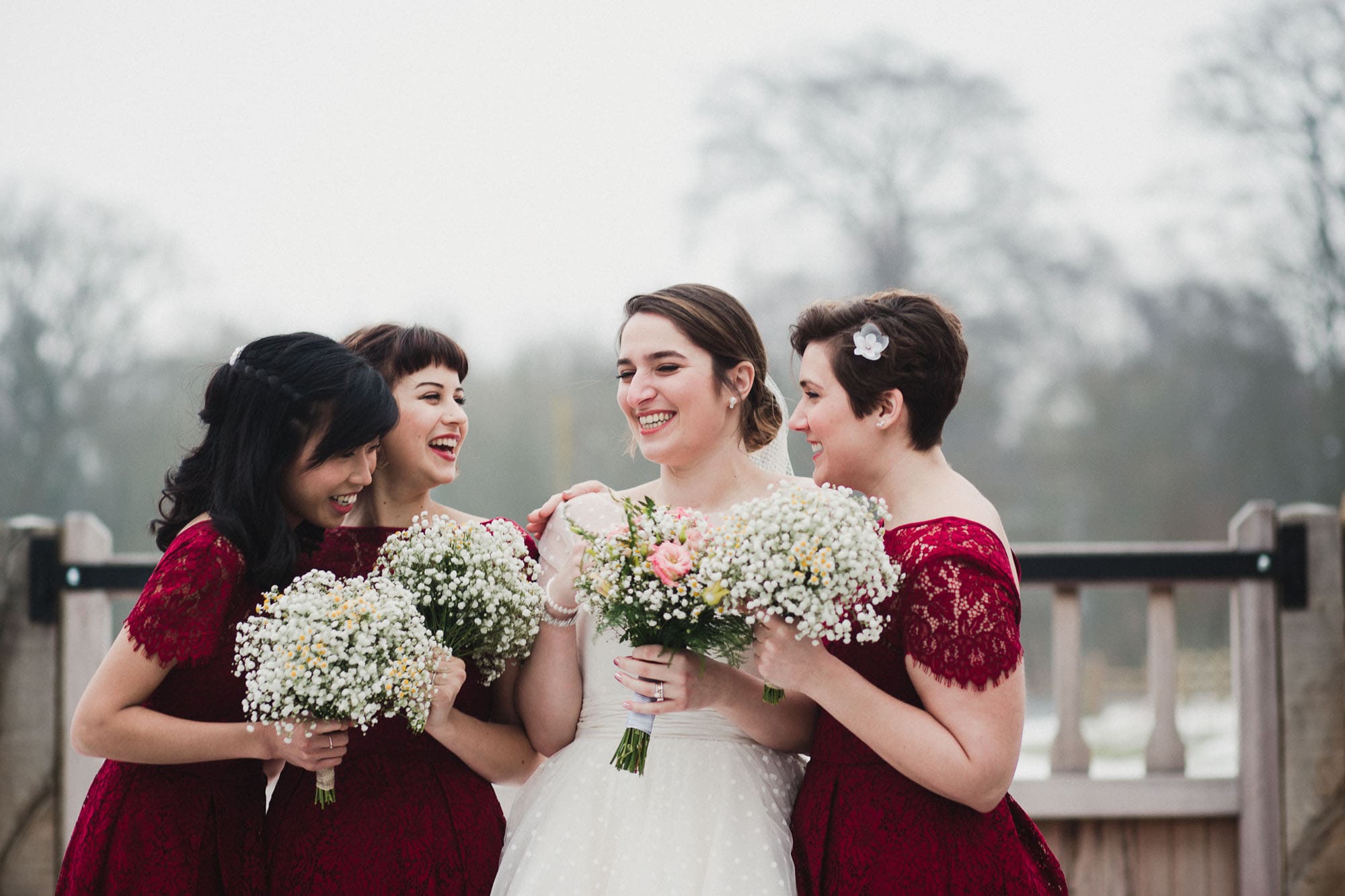 Bride and bridesmaids laughing with each other a snowy backdrop behind them.