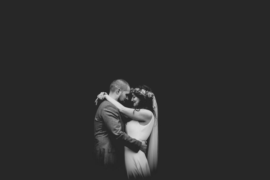 Bride and groom portrait at Hazel Gap Barn wedding venue. Black and white. Couple embrace. Bride has flower crown. Image is black and white. 