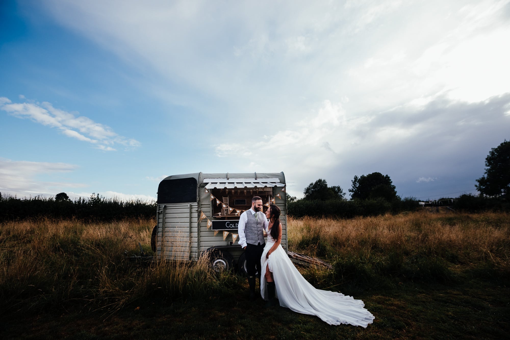 Bridge House Barn Wedding: Bethany and Mark stand in front of rustic Horse Cart surrounded by farm land