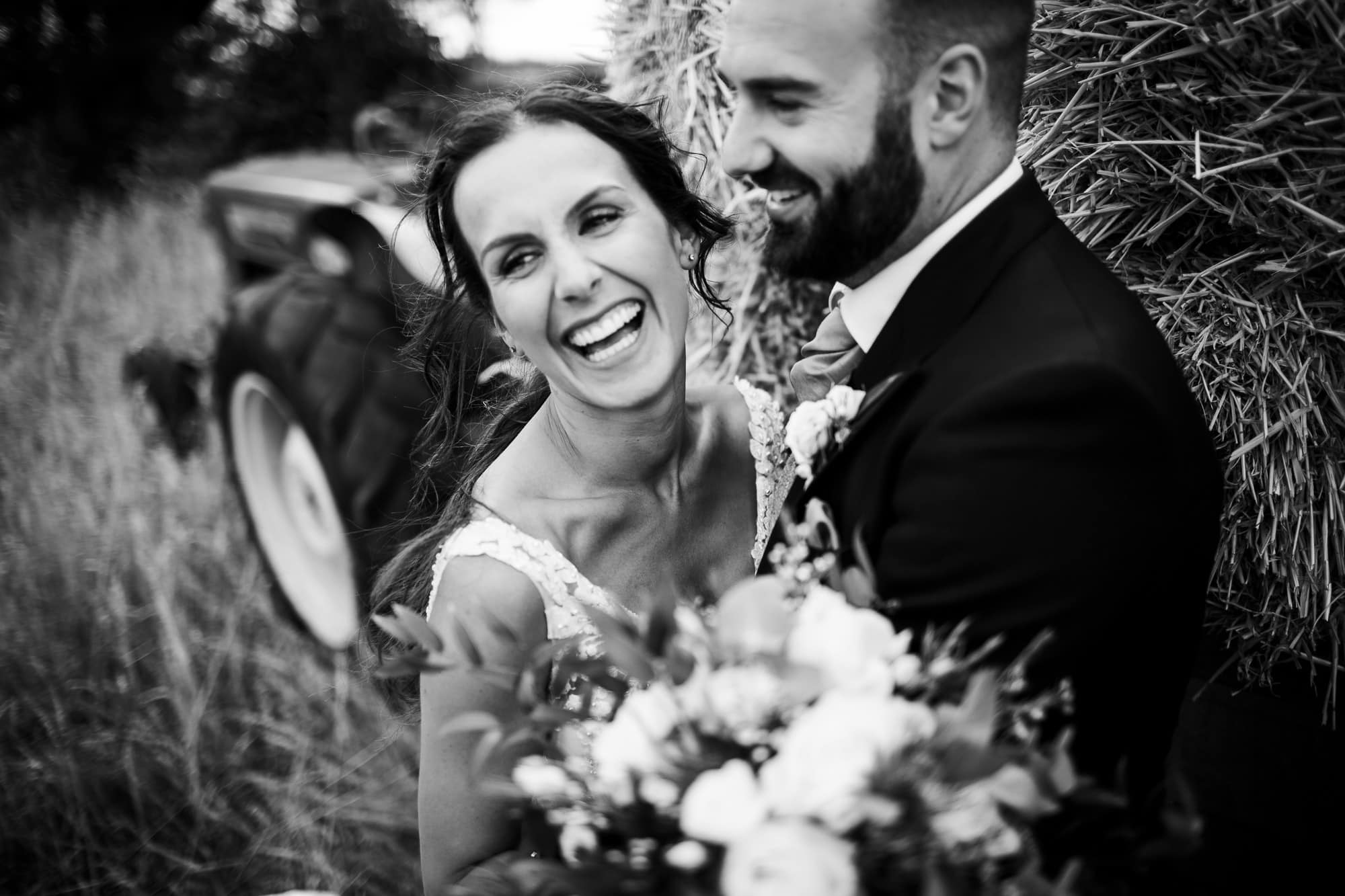 Black and white portrait of bride and groom laughing. Close up in front of hay bales at Bridge house Barn wedding