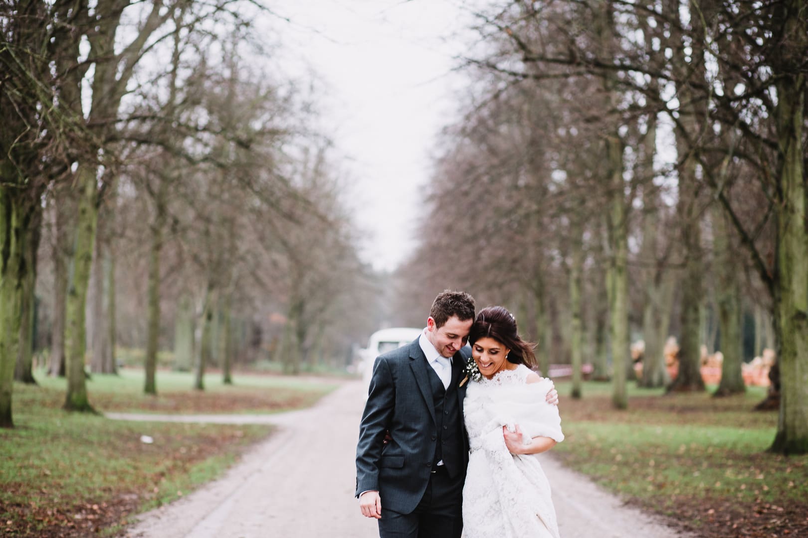 bride and groom walk down path keeping each other warm