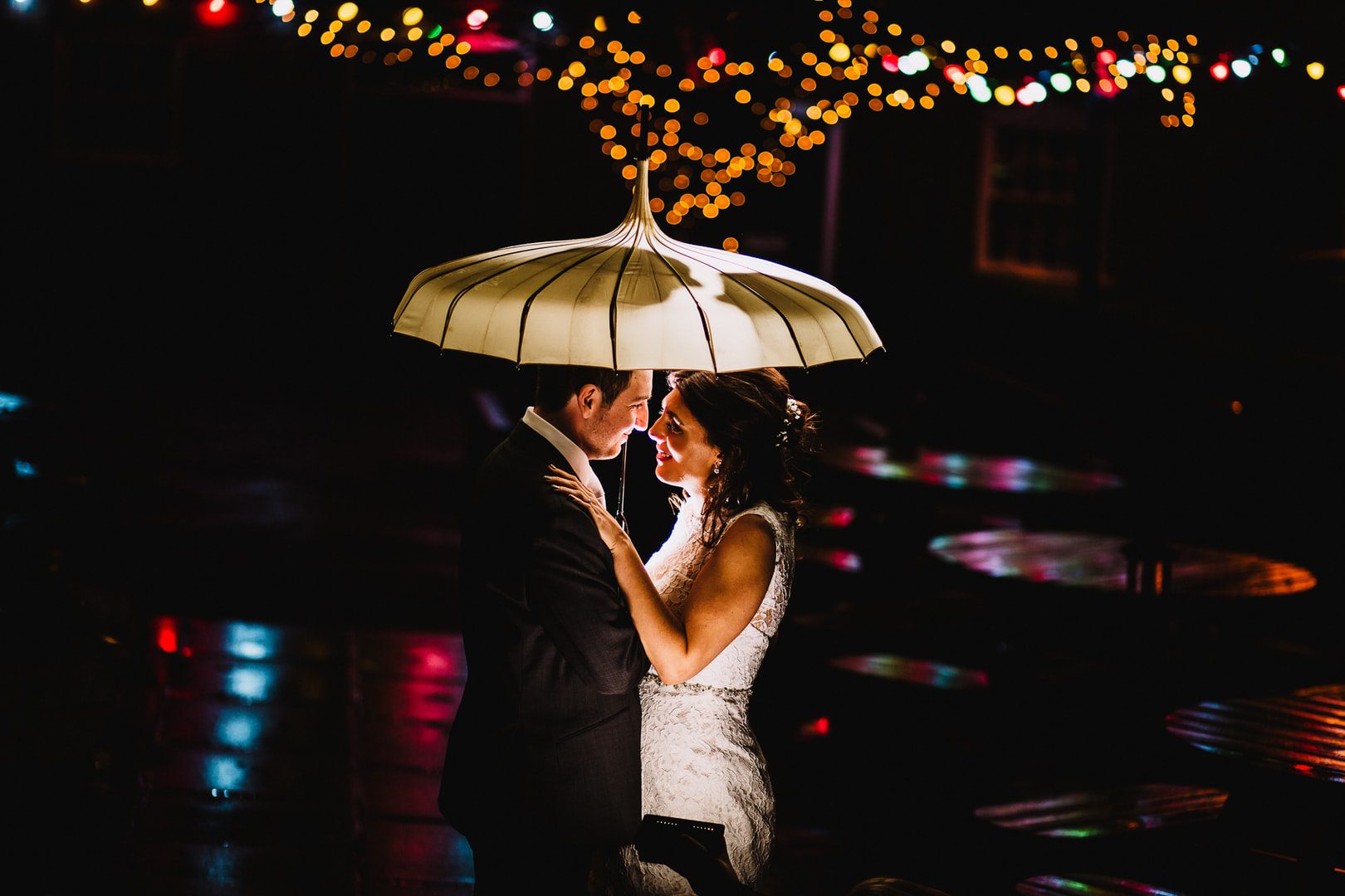 wedding photography at Rufford Mill - bride and groom under umbrella, with lights behind them