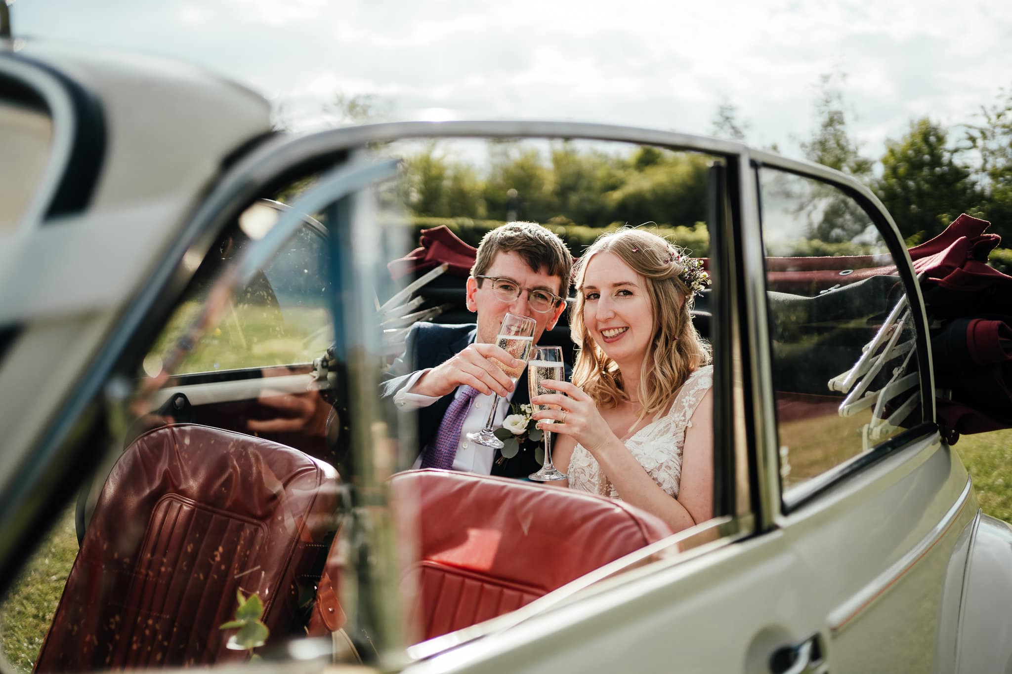 Bride and groom in the back of the vintage car with champagne