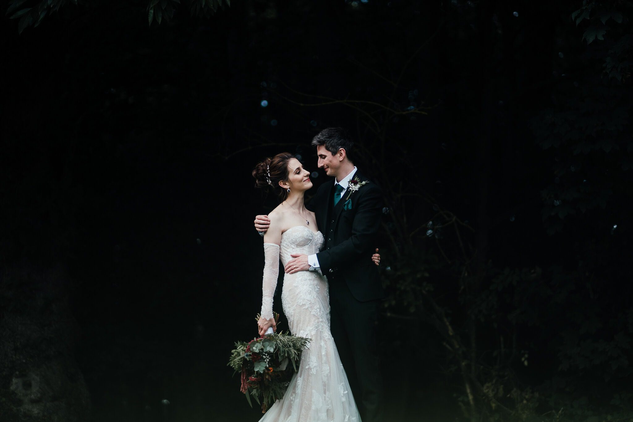 Portrait of bride and groom at Hazel Gap Barn. Being beautifully lit, with the dark woods fading to black behind them.