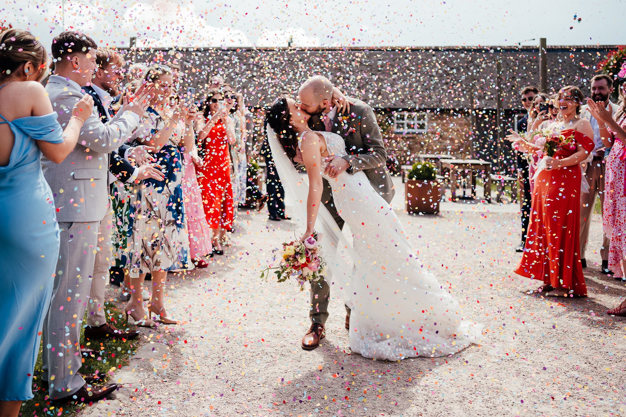 Barn Weddings in Nottingham: Couple kiss surrounded by colourful confetti at Donnington Park Farmhouse