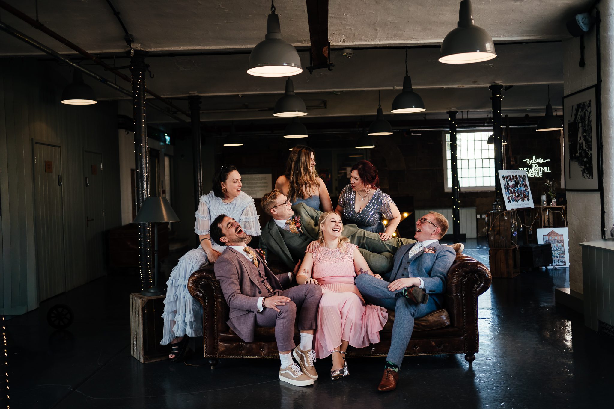 The West Mill Wedding Photographer - grooms and their best people sit on a Chesterfield at The West Mill, all laughing with each other - Friends style.