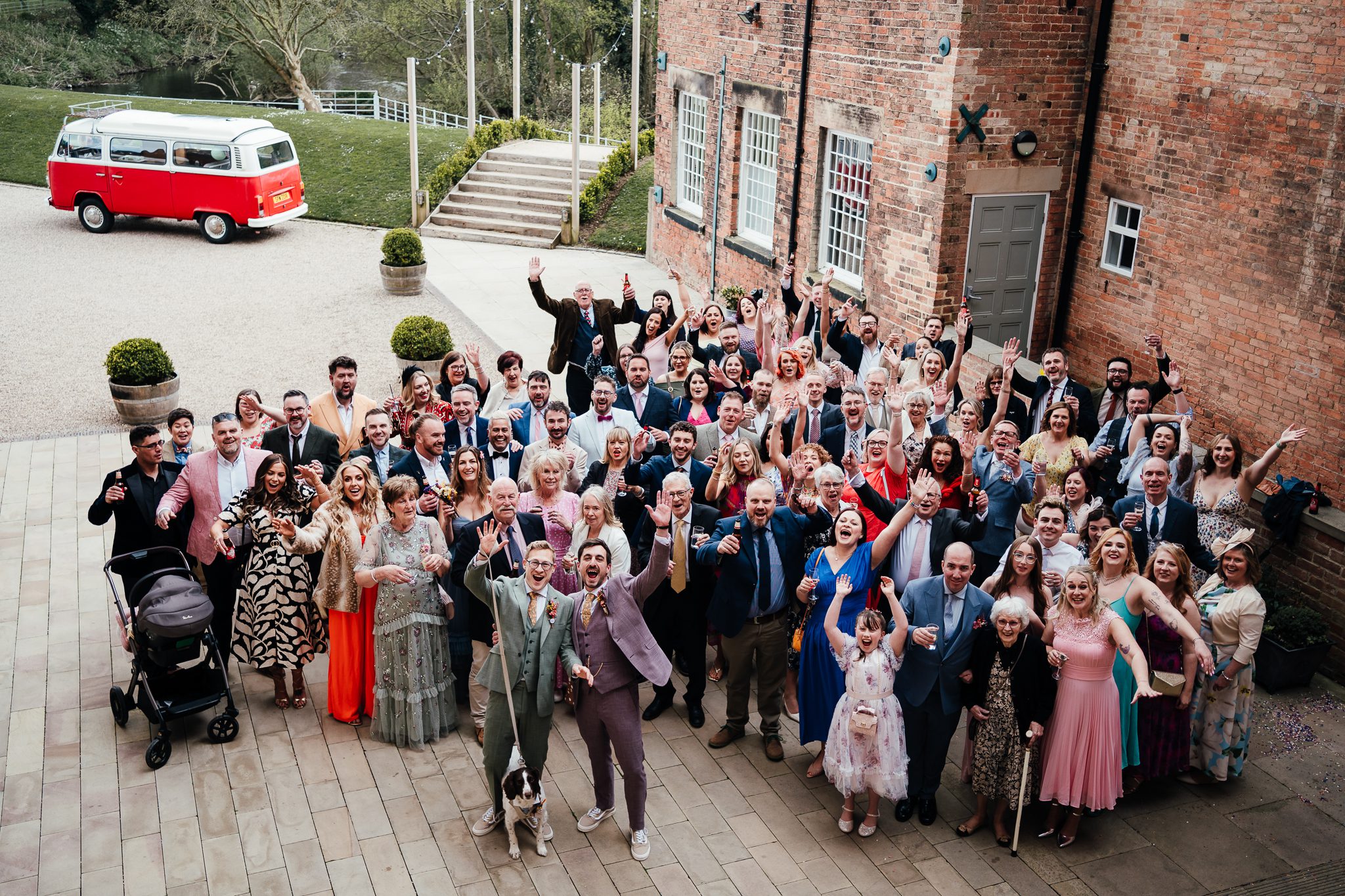 The west mill wedding photography - group photo of entire wedding party. Two grooms and their dog stand in front of all their guests. All waving up at the camera. 