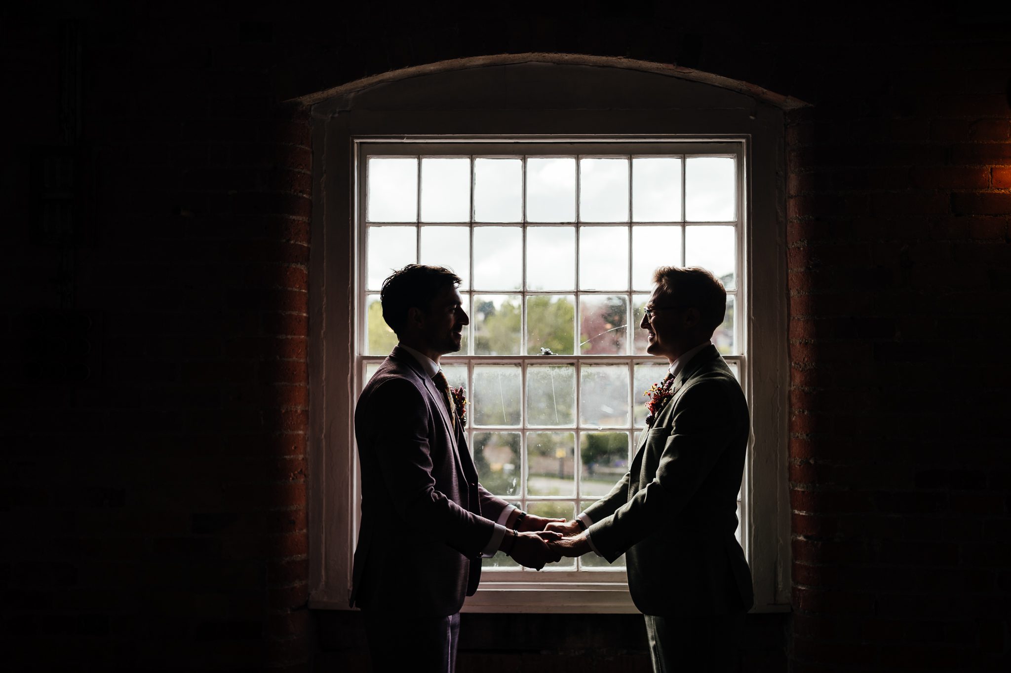 Two grooms in silhouette in front of windows at The West Mill wedding venue