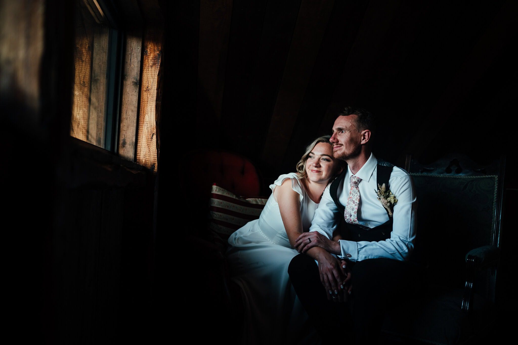 Barn weddings: Bride and groom inside the dark barn of Willow Marsh Farm, cuddled up, bathed in beautiful window light.