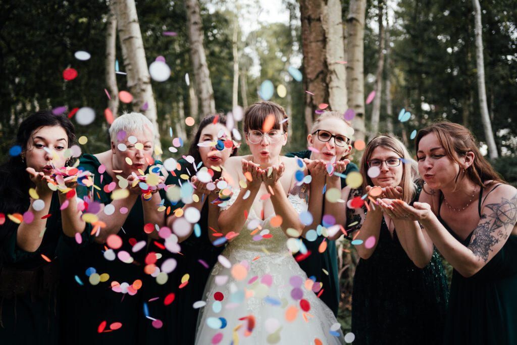 Bride and bridesmaids blow colourful confetti towards the camera