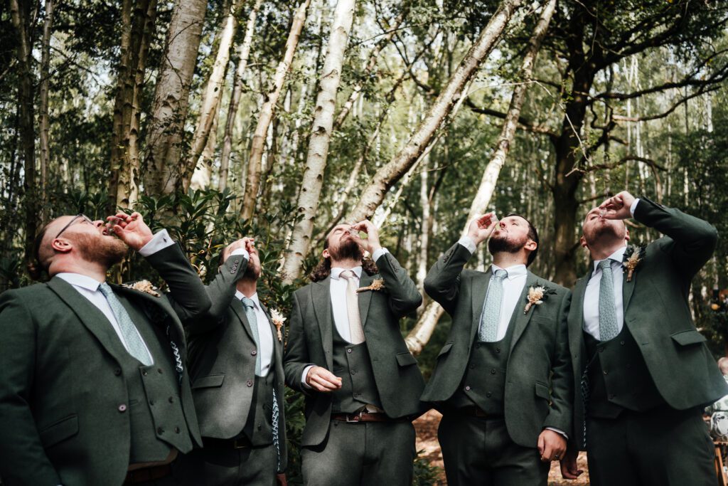 Groomsmen drink shots in woodland