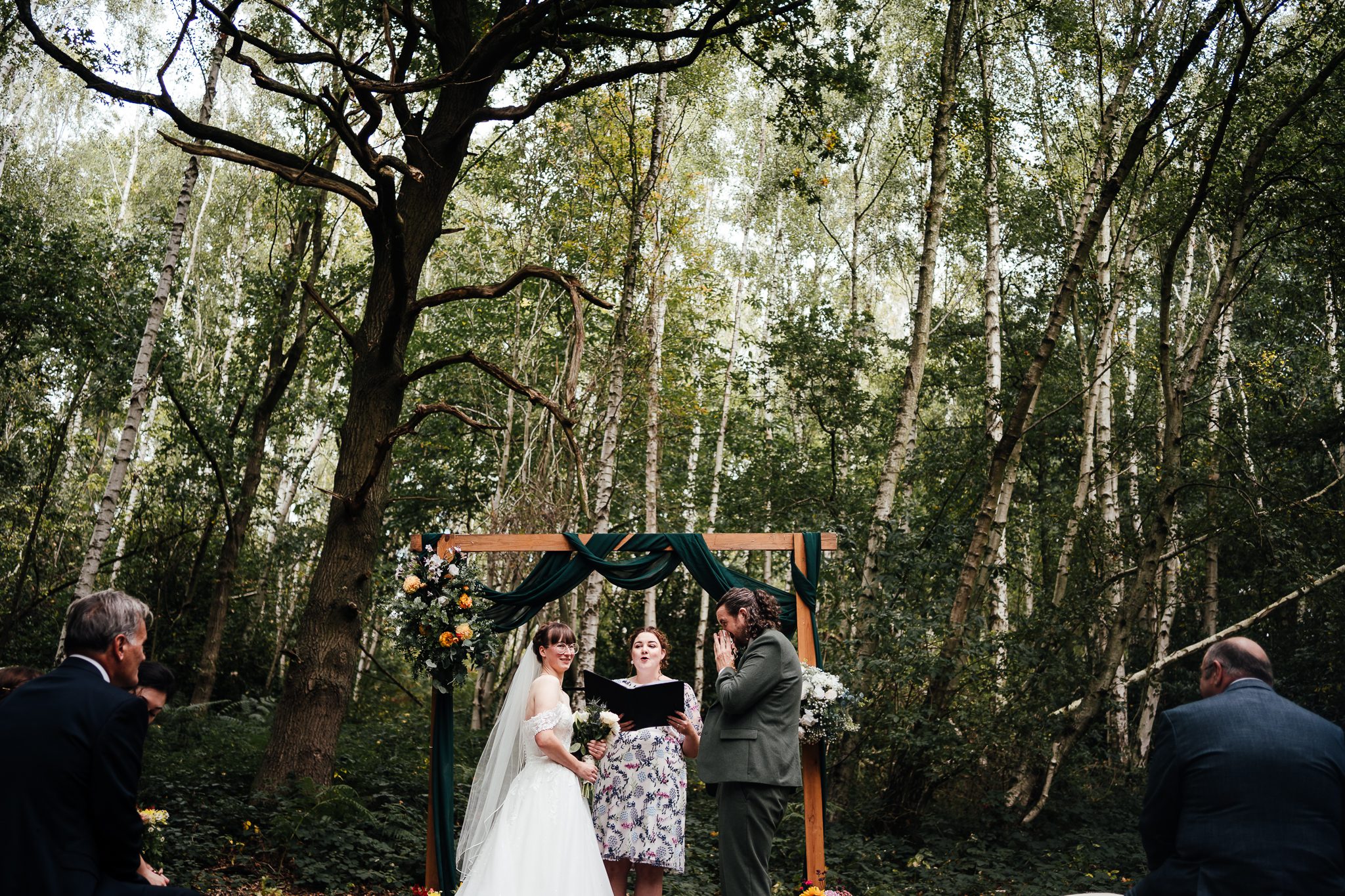 Sherwood Glade outdoor. ceremony. Bride and groom stand opposite each other in front of a backdrop of woodland