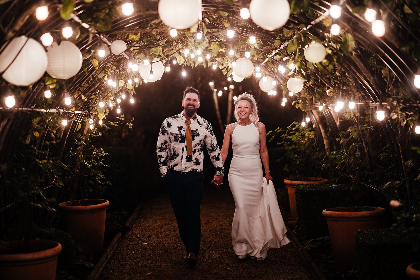 Pippley walled garden wedding photography - bride and groom walk through the archway, which is festooned with lights.