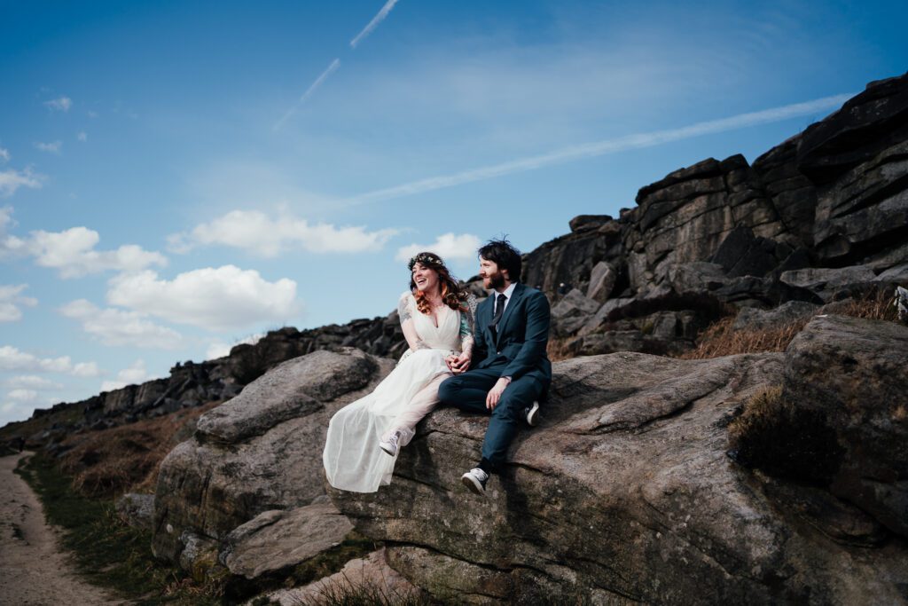 Bride and groom sit laughing on the rocks in the Peak District.