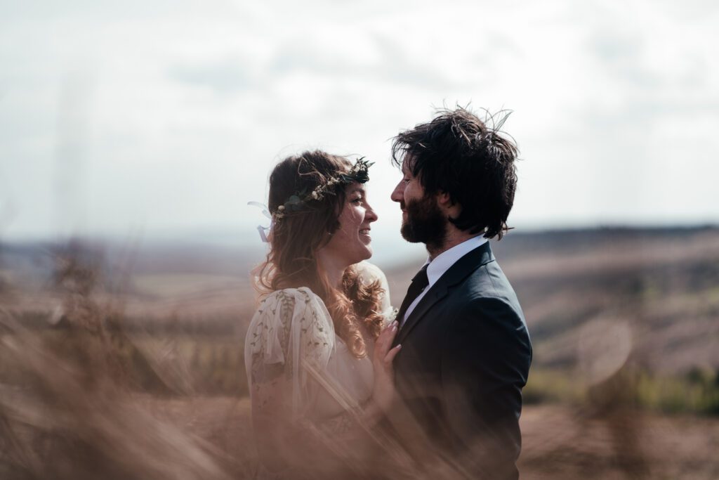 Close up of bred and groom , softly lit with sun behind them and bracken of the moors in soft focus in front of them.
