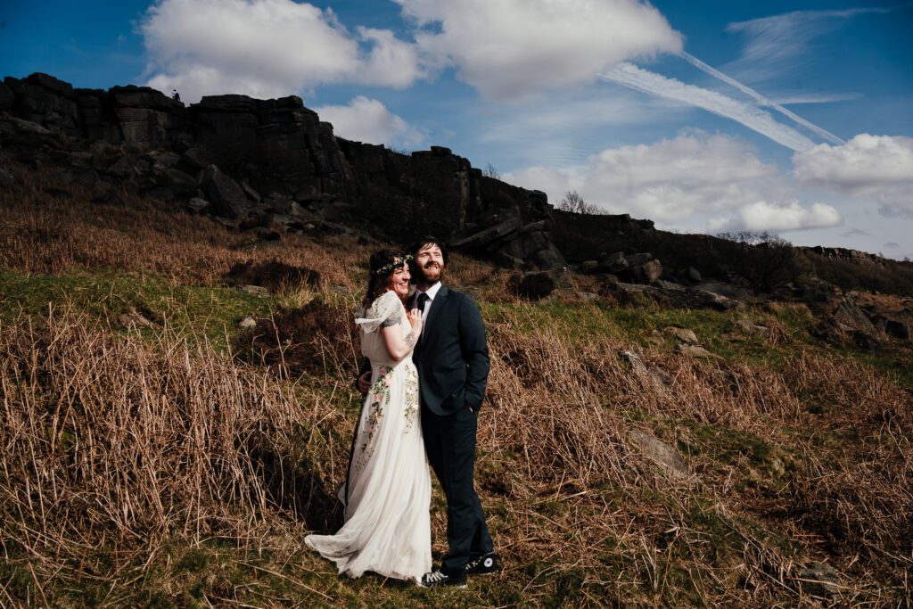 Bride and groom embrace looking out over Peak District