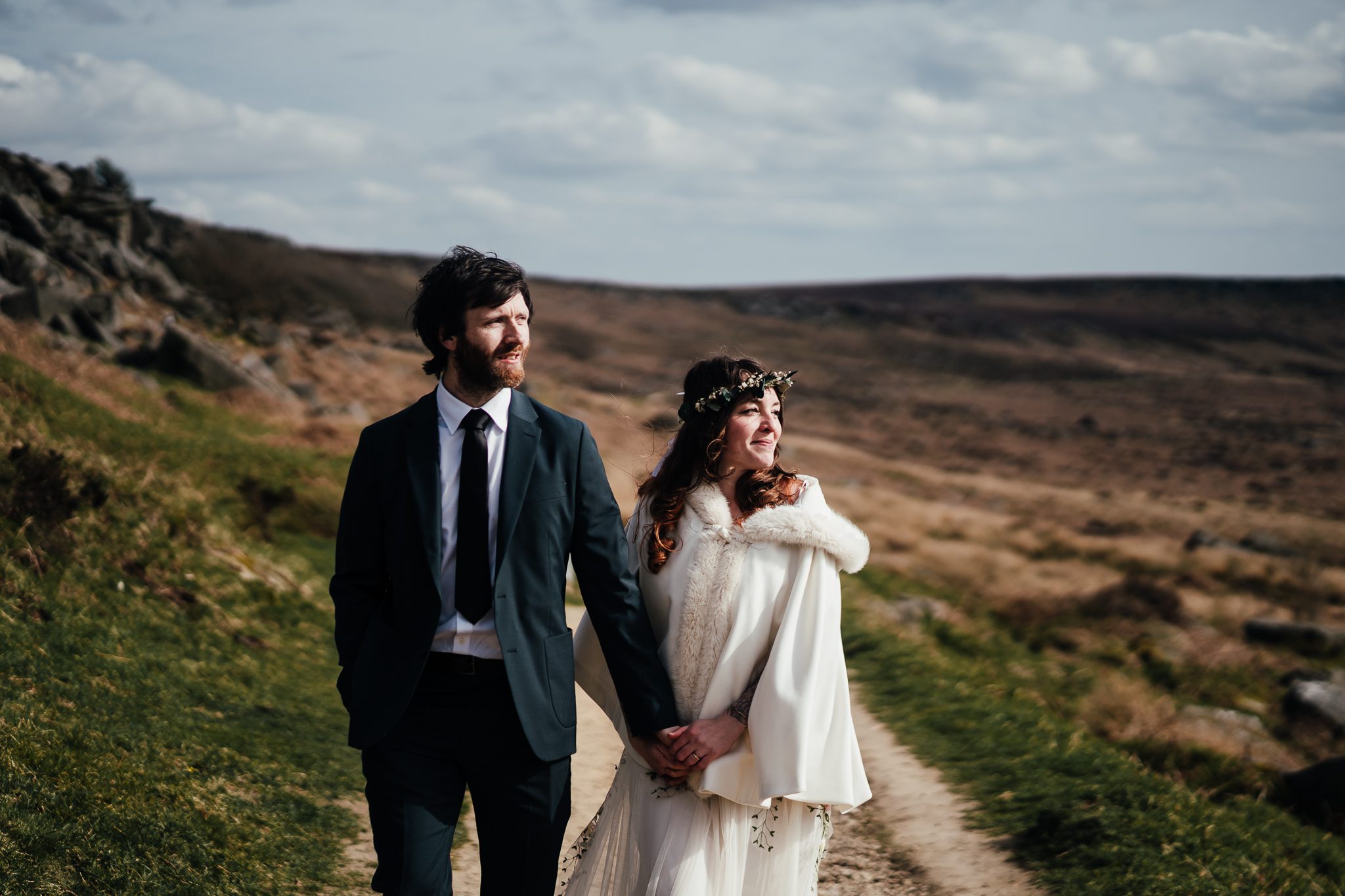 Bride and groom hand in hand walking across the landscape of Burbage in the peak district.