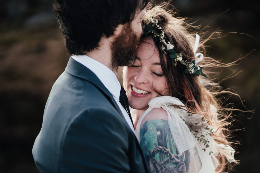 close up of bride and groom embracing. bride smiling. Groom kissing her forehead.