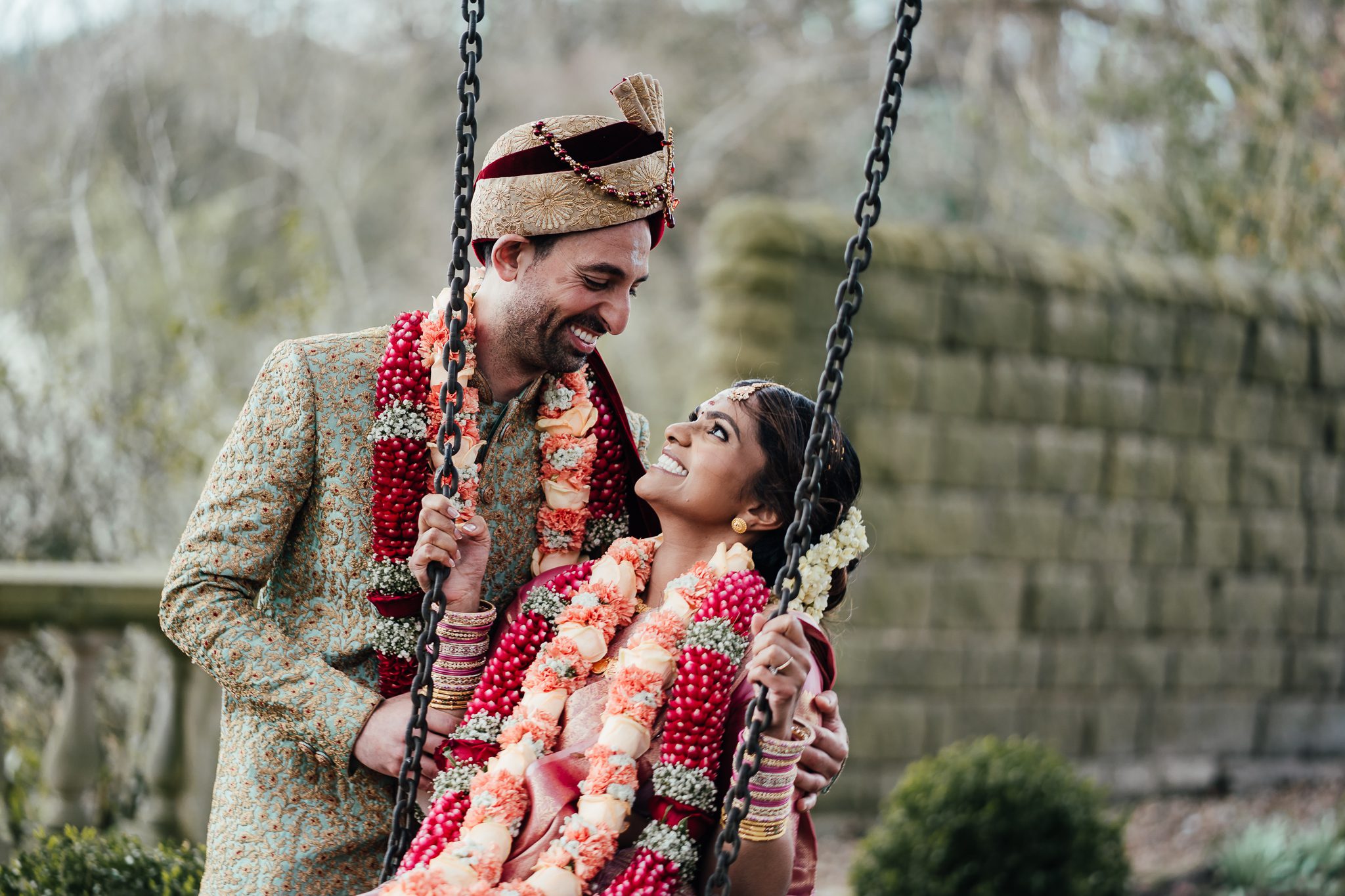 Indian wedding in the Peak District. Bride on swing, groom holds her and they look at each other.