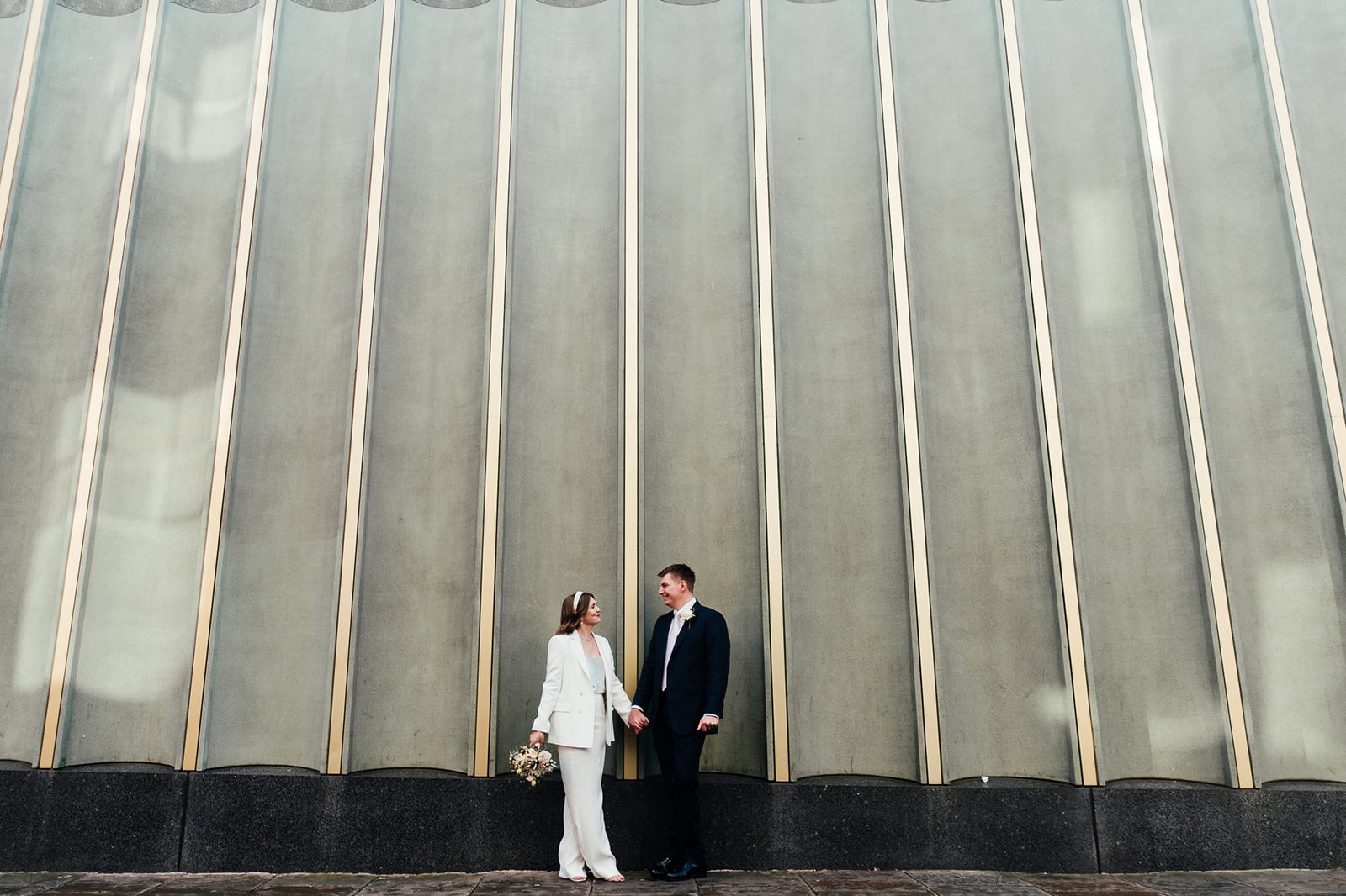 Wedding portrait outside the Nottingham contemporary art gallery. Bride in a trouser suit. holding a bouquet.