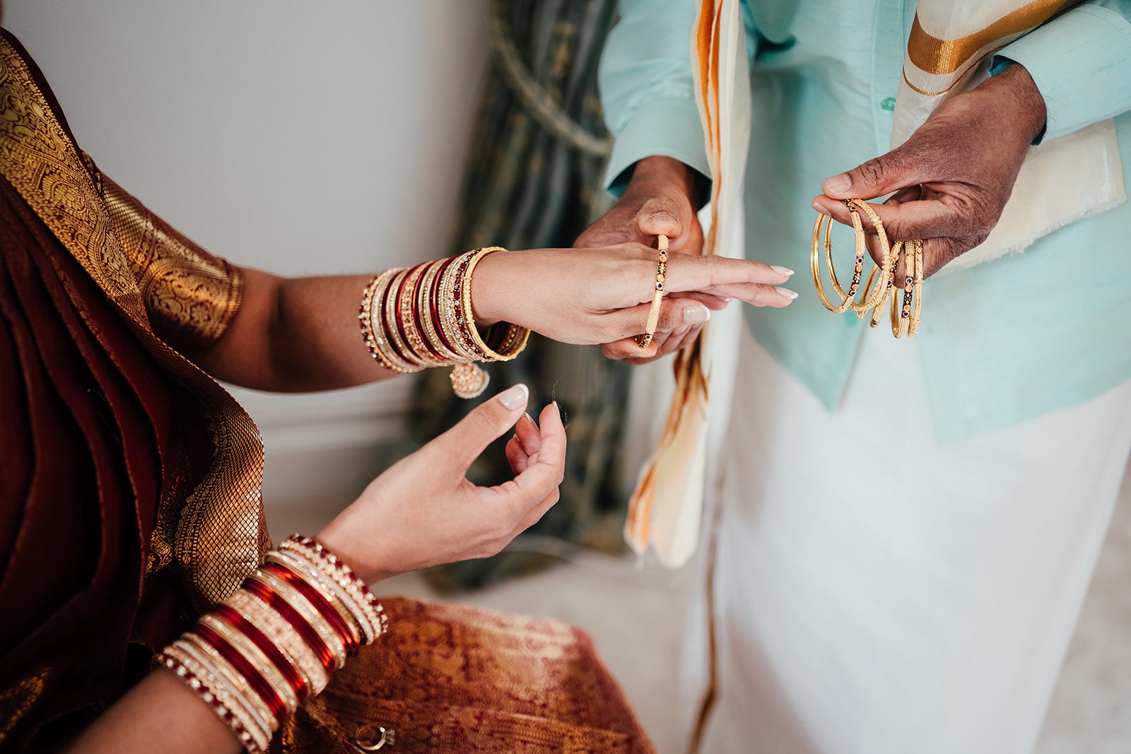 Wedding photography detail. Bride's father puts bracelets onto bride's arm. Indian wedding.
