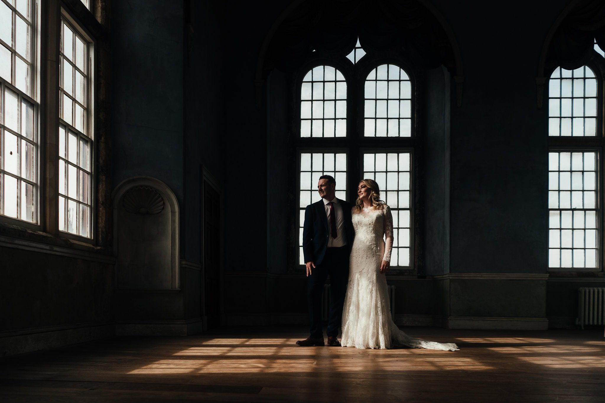 Nottingham wedding photography at Wollaton Hall Bride and groom stand in beautiful window lit room, light on their faces. Dramatic image