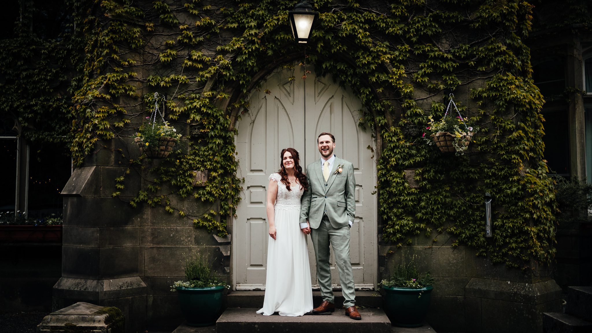 Bride and groom standing in front of the arched doorway at Hargate Hall